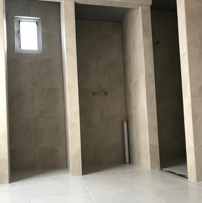 Modern bathroom under construction showcasing beige tiled walls and a designated shower area with a small window for natural light